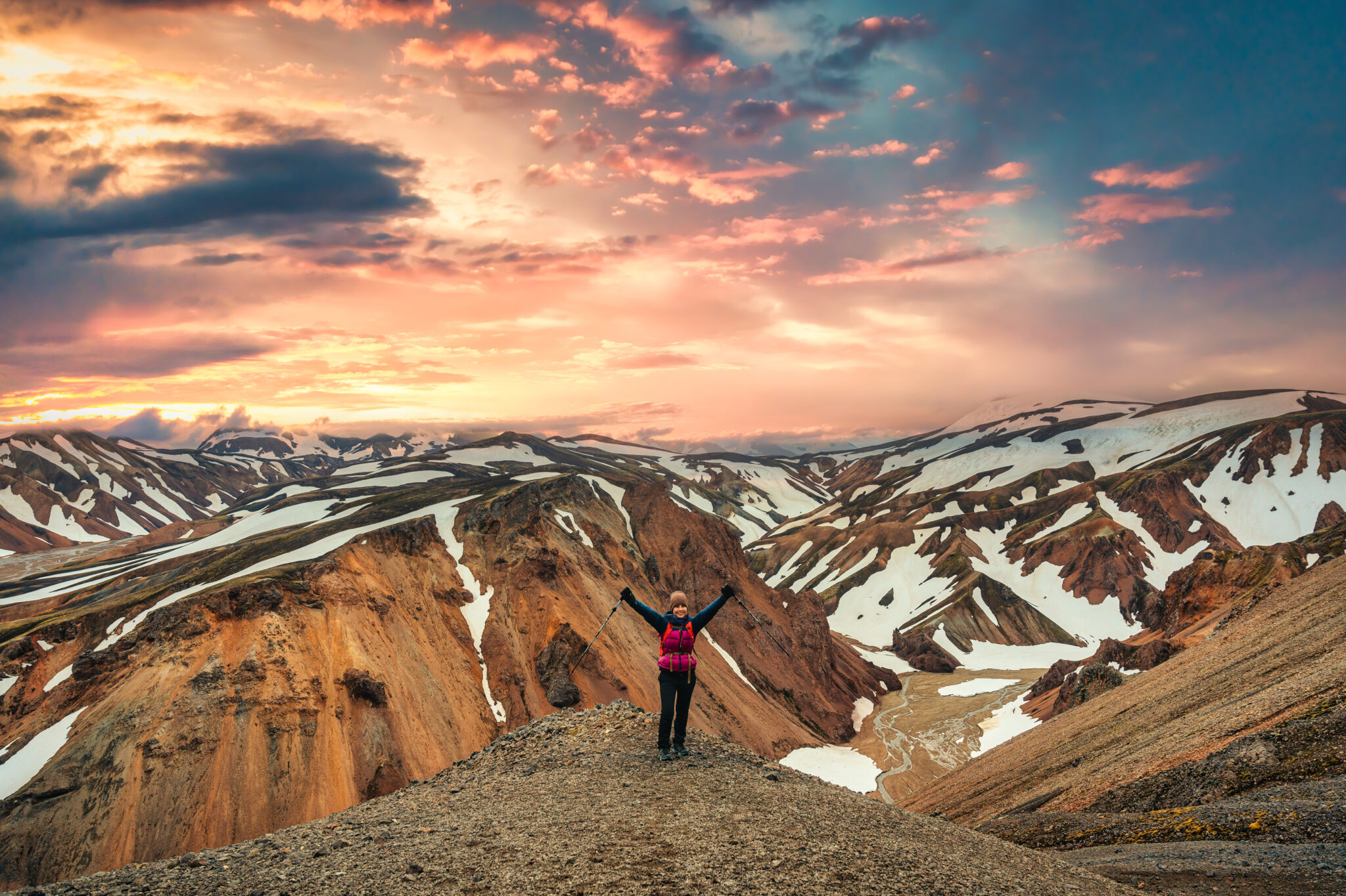 Cheerful hiker woman standing on the peak with volcanic mountain range with snow covered on Blanhjukur trail in summer at Landmannalaugar, Iceland