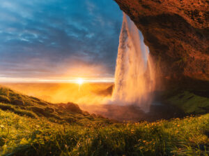 Panorama of beautiful Seljalandsfoss waterfall flowing and midnight sunset shining on flower garden in summer at South of Iceland