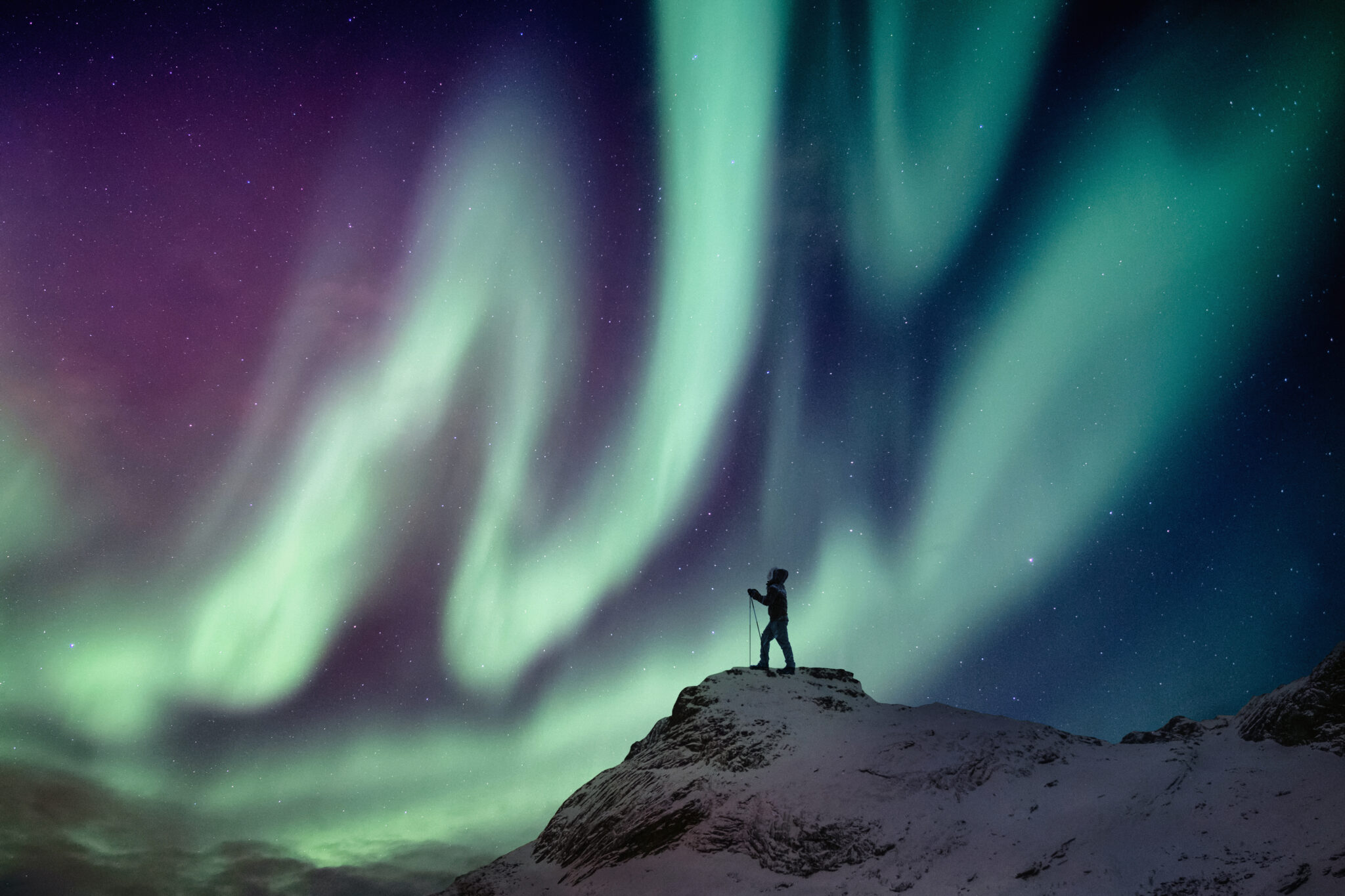 Man climber standing on snowy peak with aurora borealis and starry in the night sky