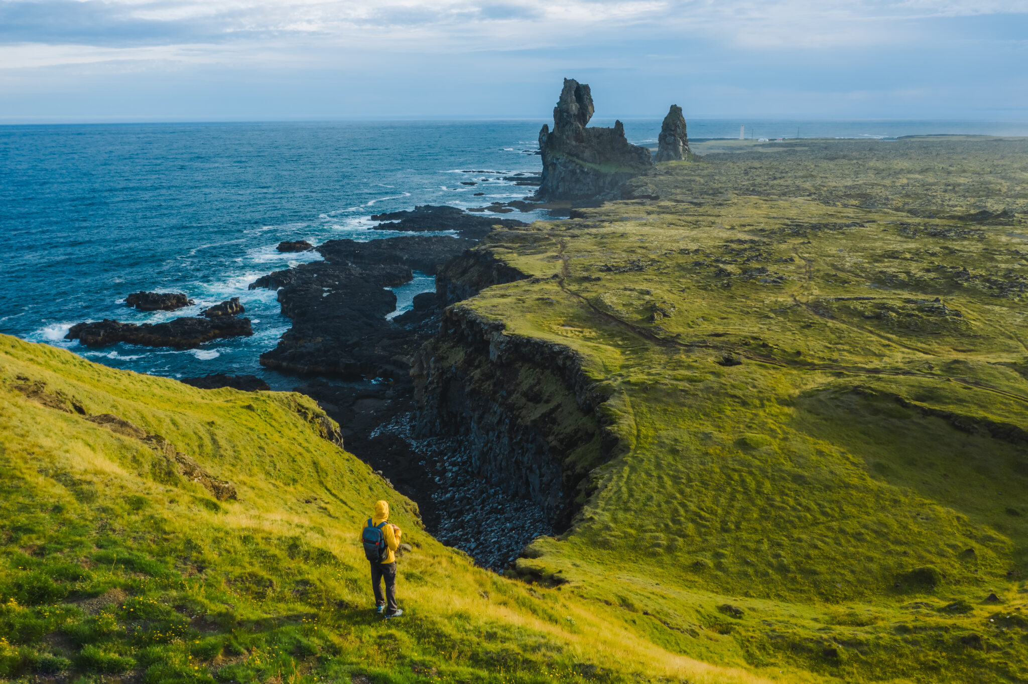 Man hiker in yellow jacket stand on the peak of the rock in outdoor park in Iceland. Londrangar.
