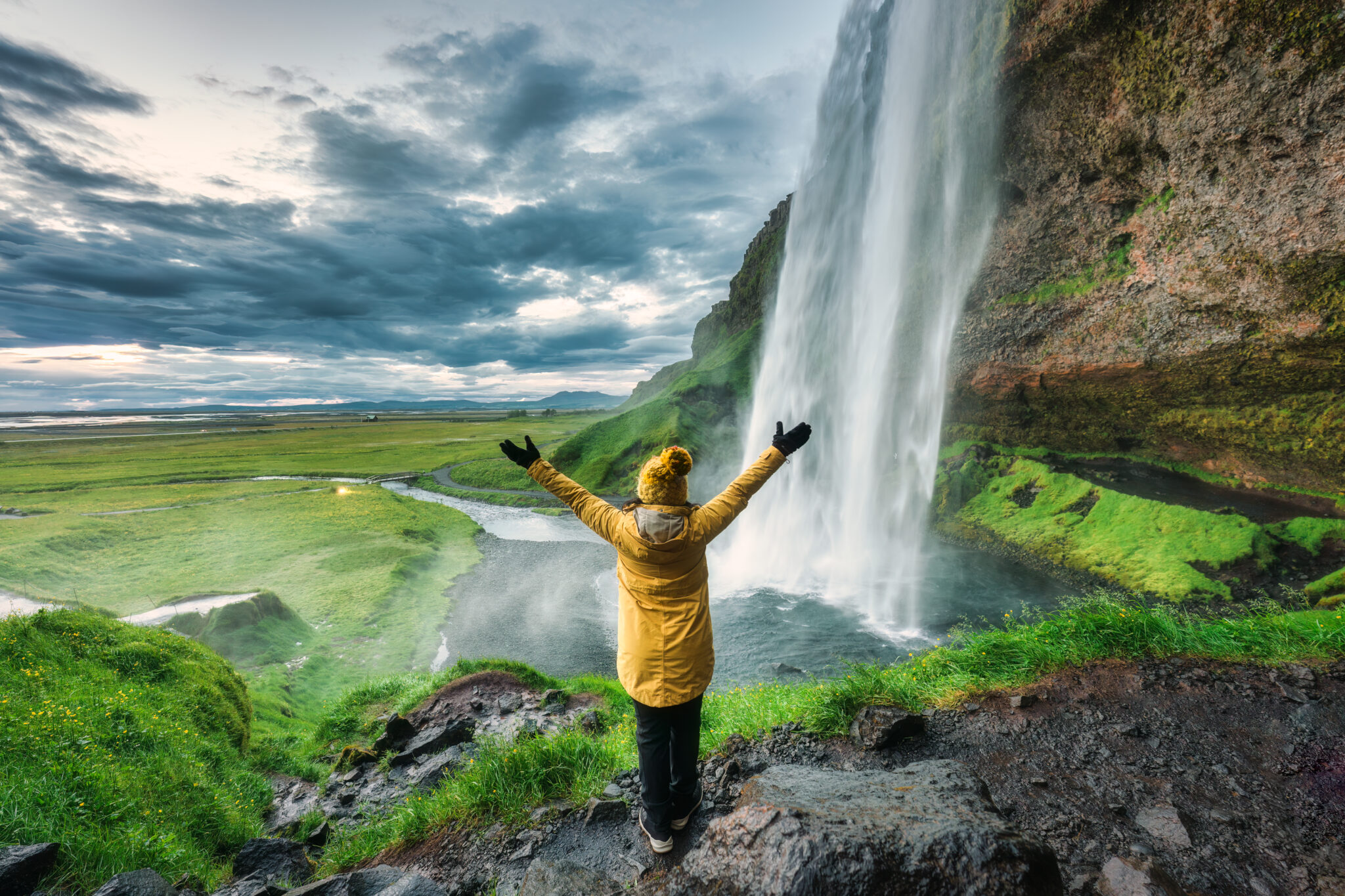 Beautiful Seljalandsfoss waterfall flowing from cliff with cheerful tourist woman standing in summer at South of Iceland