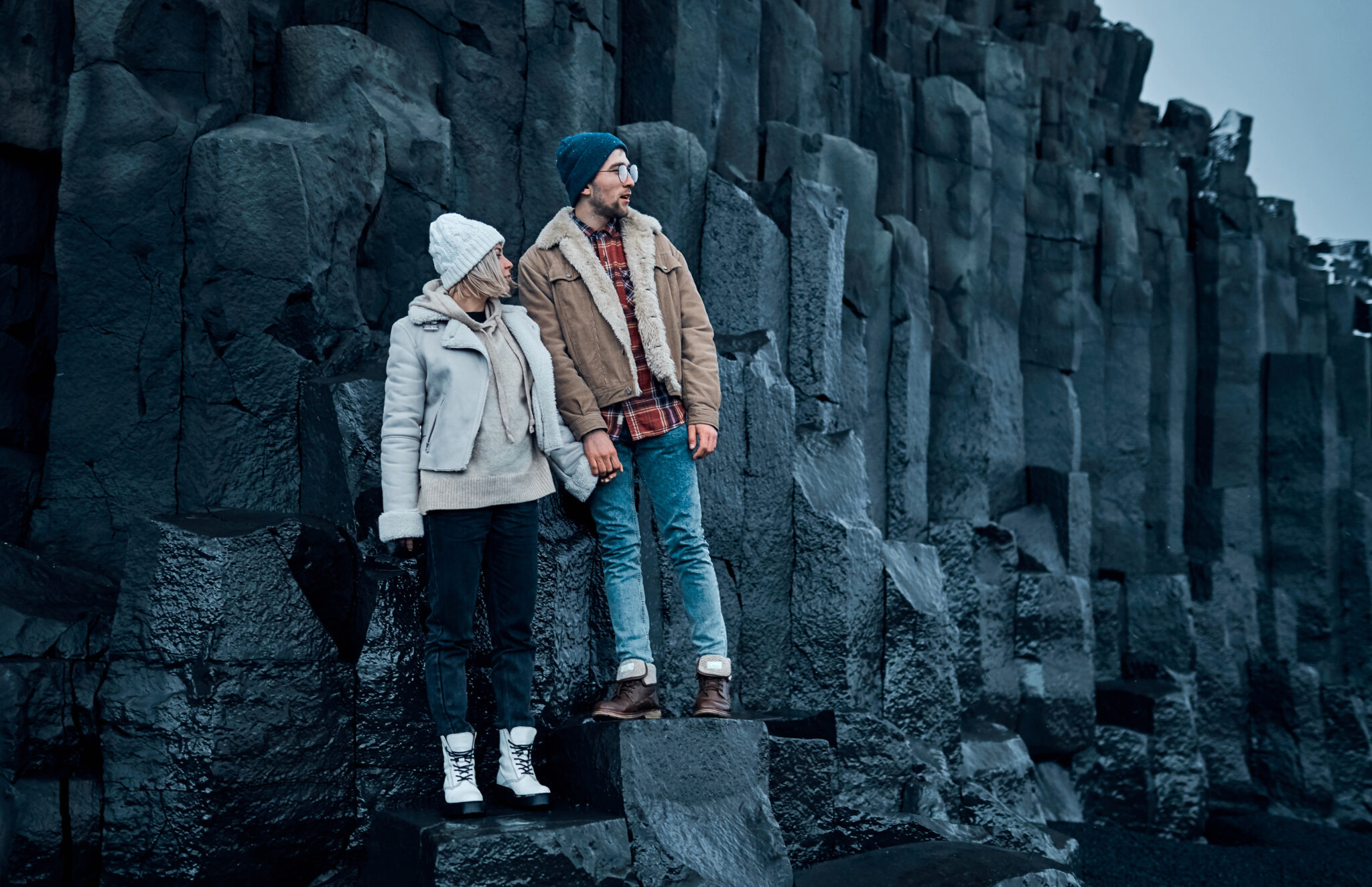 Loving couple of tourists stand holding hands on the stones of black volcanic basalt mountains. Travel, recreation, tourism.