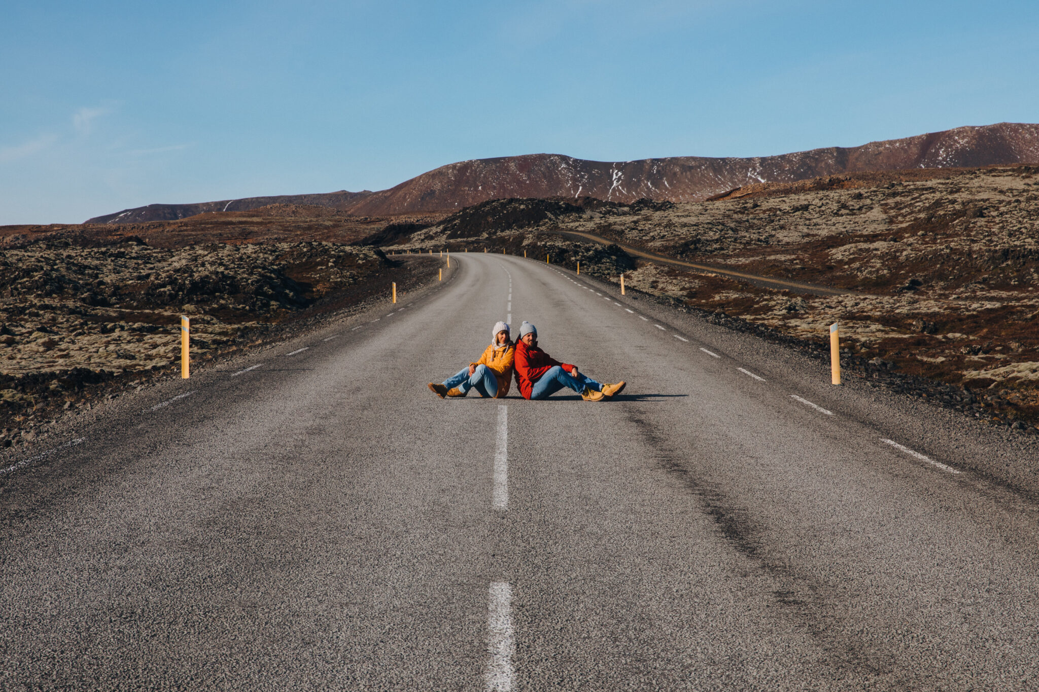 young couple sitting on asphalt road with beautiful icelandic landscape behind, reykjanes, iceland